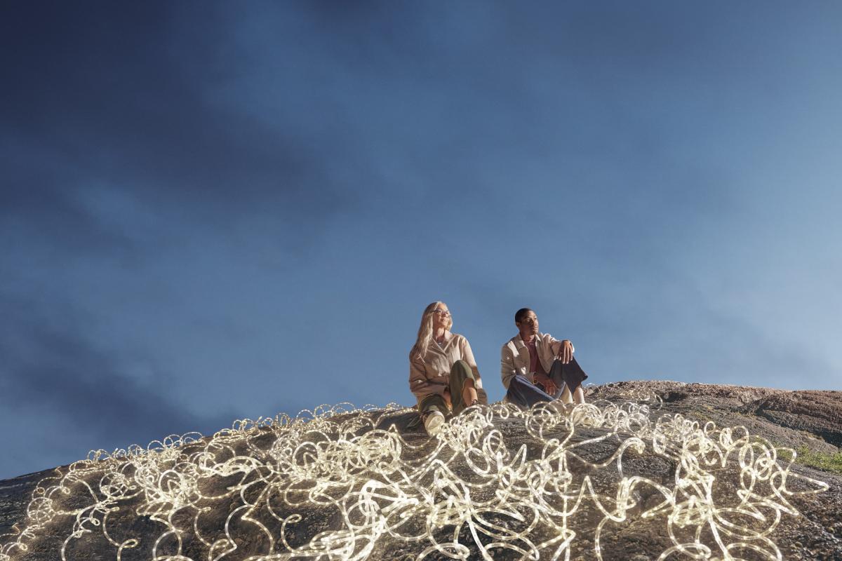 Expansive dark blue-sky backdrop, with a man and woman in the foreground surrounded by white LED rope lights.